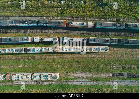 Aerial top down view of many old, abandoned trains sitting on numerous tracks in a large, green railway depot during the day Stock Photo