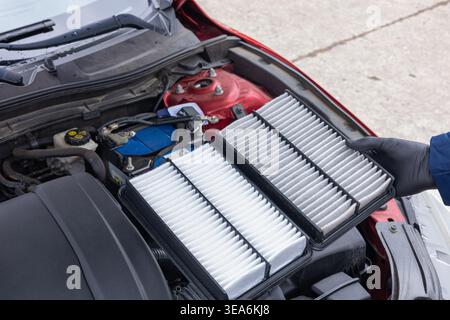 Replacing engine air filter in car during maintenance showing clean and used filter comparison Stock Photo