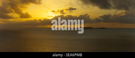 Aerial view of the island of Praslin at sunset with golden light rays breaking through dark clouds over the calm Indian Ocean in Seychelles. Stock Photo