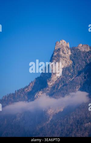 Rocks of the Rötelstein at Lake Traunsee with atmospheric clouds against a bright blue sky Stock Photo