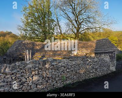 Stone outbuilding with sagging stone slate roof behind dry stone wall in Tideswell, Peak District National Park, Derbyshire, England, UK Stock Photo
