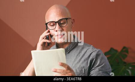 Businessman On Phone Reviewing Notes In Modern Office Setting With Focused Expression Stock Photo