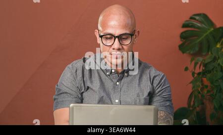 Focused Professional Man Working on Laptop in Modern Office With Plants and Casual Business Attire Stock Photo