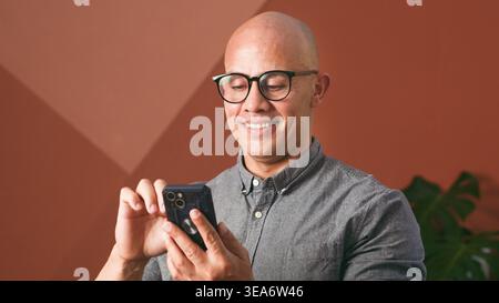 Smiling Businessman Using Smartphone in Casual Office Setting for Remote Work and Communication Stock Photo
