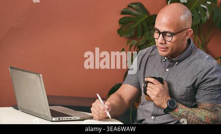 Businessman Working Remotely With Laptop And Coffee Taking Notes In Modern Home Office Stock Photo