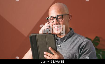 Businessman Talking on Phone While Reading Tablet Content in Home Office Setting Stock Photo