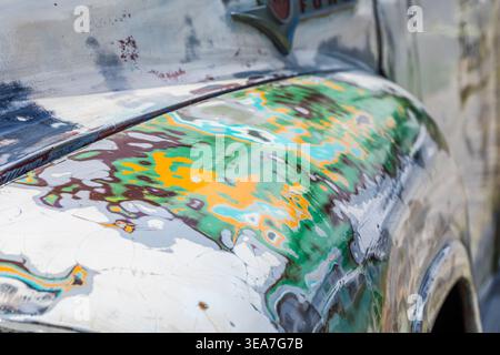 Close-up of a weathered car body with peeling paint and rust, showing detailed texture and decay on an old vehicle surface. Stock Photo
