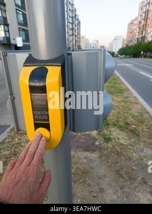 Hand pressing yellow crosswalk button on a traffic light pole for pedestrian crossing Stock Photo