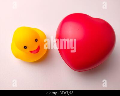 Yellow rubber duck placed next to a large red heart on a clean white background. Stock Photo