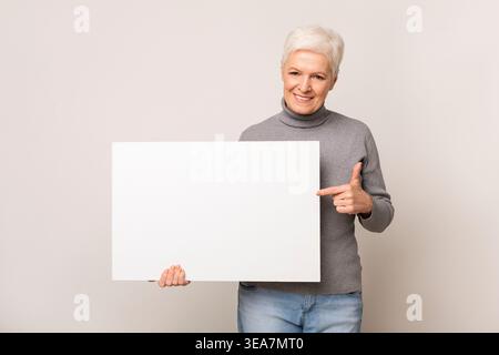 Senior Woman Smiling and Holding a Blank Sign Against a Neutral Background Stock Photo