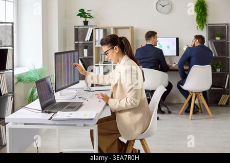 Business analyst woman working on spreadsheets at desktop in bright open office Stock Photo