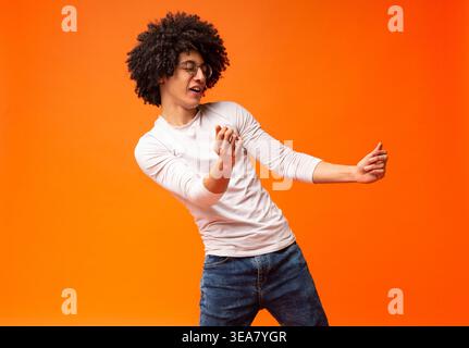 Flexible millennial black guy dancing on orange background Stock Photo