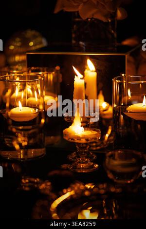 Floating tea lights and white candles in glass holders on table Stock Photo