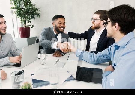 Happy team congratulating successful worker by shaking hands Stock Photo