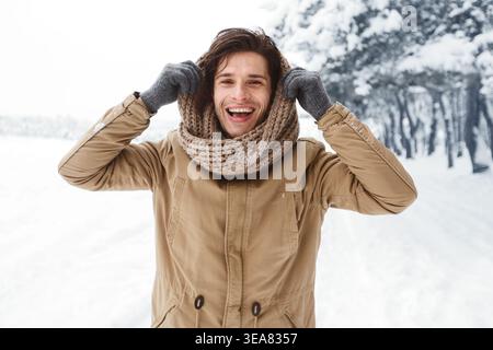 Handsome Man Pulling Scarf On Head Standing In Snowy Forest Stock Photo