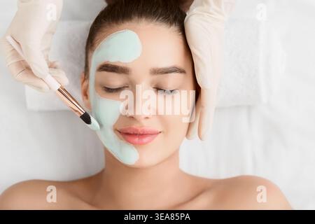 Beautician Applying Clay Face Mask On Woman Face Stock Photo