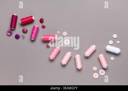 Different pink thread spools and buttons on grey background Stock Photo