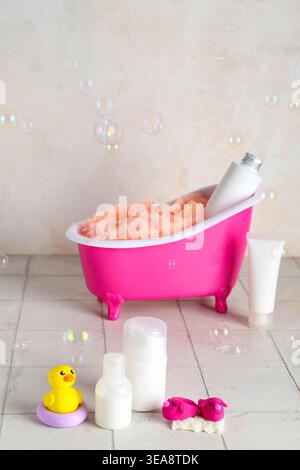 Small bathtub, cosmetic products and soap bubbles on light tile table Stock Photo