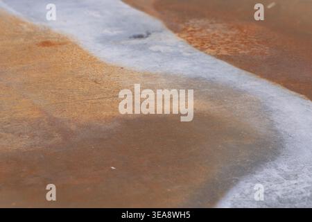 Abstract macro texture of rusty metal and grey cement surface showing orange corrosion lines and grainy industrial background style. Stock Photo