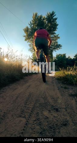 Cyclist rides mountain bike sunset trail rural field. Back view. Riding on bike in the countryside. Biking outdoor sport activity. Young man enjoying Stock Photo