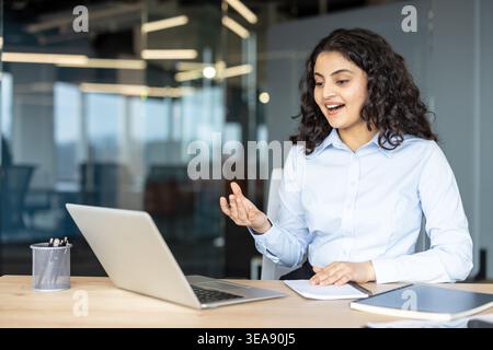 Indian businesswoman using laptop for online meeting at office desk, actively communicating and gesturing during a virtual conference, connecting with remote colleagues Stock Photo