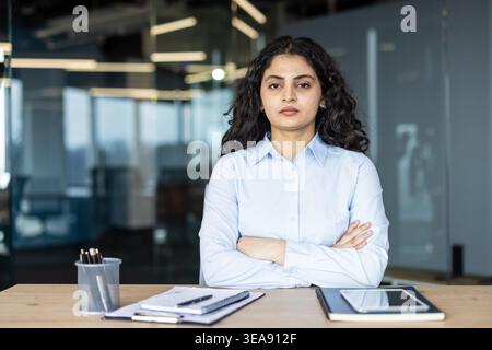 Young middle eastern businesswoman standing confidently with arms crossed, looking directly at the camera, showing professionalism and determination in a corporate office environment Stock Photo