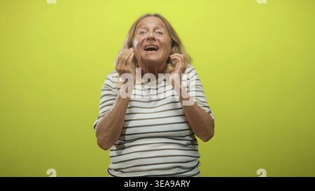 Senior woman laughing with hands clasped near chest and touching face in studio; joyful contentment. Stock Photo