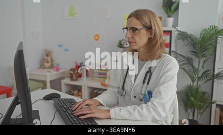 Woman pediatrician types on keyboard with hands on keys, stethoscope visible in clinic building; calm child care. Stock Photo