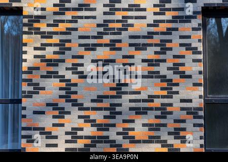 Modern Patterned Brick Wall Building Facade. Front view of a contemporary brick wall with gray, black, and orange blocks, creating a geometric Stock Photo