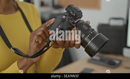 Woman adjusts camera with hands and taps dials on lens while holding strap in studio; concentration craft practice. Stock Photo