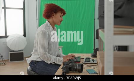 Woman typing on keyboard beside a dslr camera on the table in studio, using monitor and control panel for editing and color grading; creative concentr Stock Photo