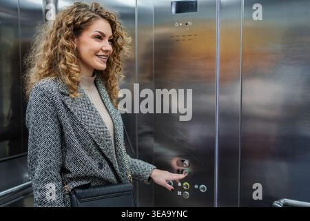 Smiling woman pressing elevator button in office building Stock Photo