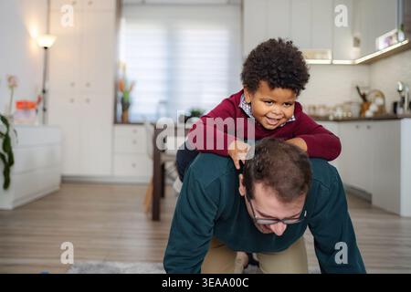 Father giving piggyback ride to happy son at home Stock Photo