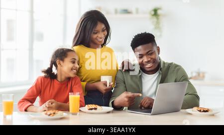Family Enjoys Breakfast While Watching Something on a Laptop in the Kitchen Stock Photo