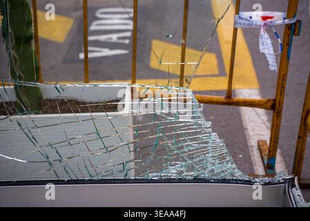 Close up of shattered safety glass with cracks and fragments on a broken window near a street barrier and road markings. Stock Photo