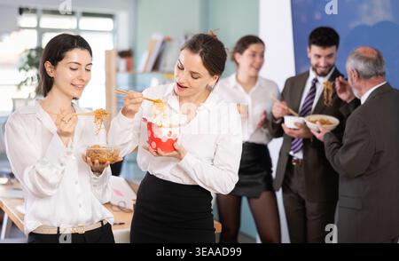 Office workers are eating noodles during their break and chatting with each other Stock Photo