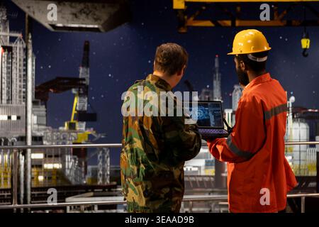 Offshore engineer and naval officer using AI technology on laptop to inspect drilling operations, working with the maritime command post to ensure oil extraction activity. Coastal defense. Stock Photo
