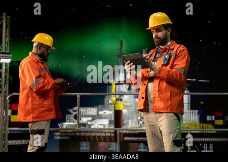 Drilling ship engineer using tablet to control subsea systems during aurora borealis night. Worker monitoring anomaly detection using device on offshore platform under northern lights Stock Photo