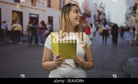 Woman holding yellow book, hands visible and smiling while reading on street; curiosity learning joyful. Stock Photo