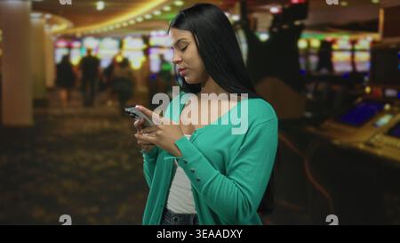 Woman holding smartphone while standing on patterned carpet in brightly lit casino slot machine area; concentration. Stock Photo