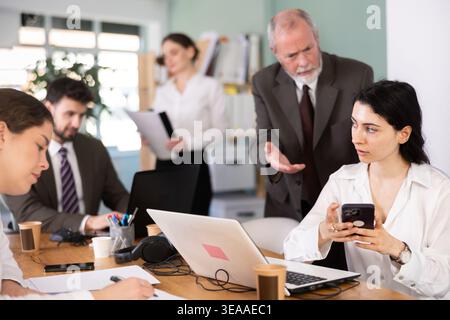 Senior manager scolds young female employee for talking on mobile phone while working in office Stock Photo