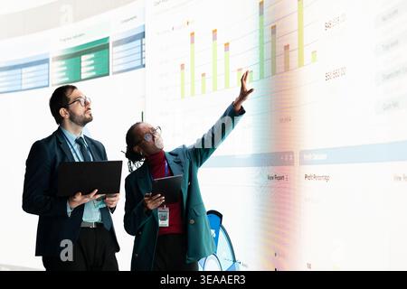 Businesspeople looking at charts projected on digital wall, verifying company financial statements, doing brainstorming. Teamworking colleagues use devices to analyze economic data graphs on dashboard Stock Photo