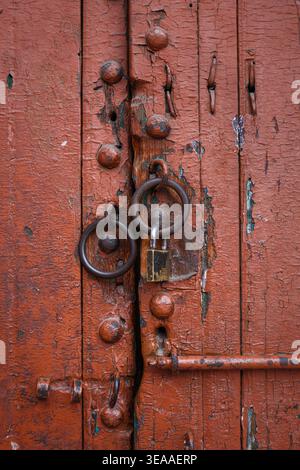 Old rusty padlock on cracked red wooden door. Marrakesh, Morocco. Stock Photo