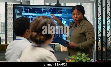System administrator presents AI chatbot reducing work volume to executives. African american startup IT specialist analyzing business insights for management using artificial intelligence, camera B Stock Photo