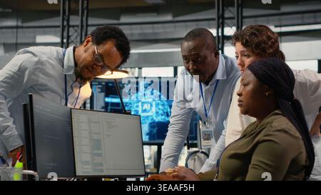 Team of technicians in office working together, automating workflows using AI. IT specialists collaborating to refine machine learning computational models for faster processing, camera B Stock Photo