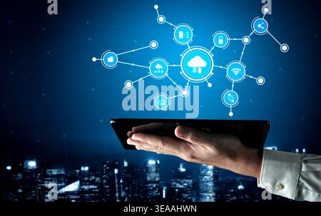 A hand holds a tablet displaying a digital cloud icon with various connectivity symbols. This image represents technology, networking, and data Stock Photo