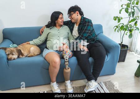 Pregnant woman with prosthetic leg and partner relaxing on sofa with their dog Stock Photo