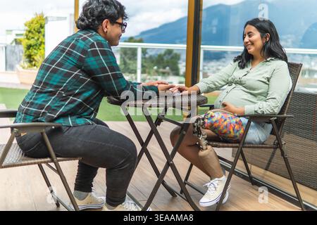 Couple sharing a tender moment, a pregnant woman with a prosthetic leg holding hands with her partner Stock Photo