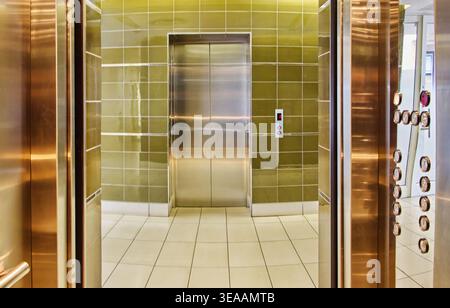 The view from inside an open elevator reveals a stainless steel control panel and handrail looking toward another set of closed lift doors in a green Stock Photo