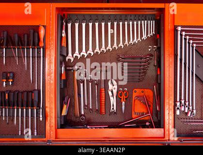 wall-mounted orange metal tool cabinet features a variety of neatly arranged hand tools including wrenches, screwdrivers, hammers, and pliers on a peg Stock Photo